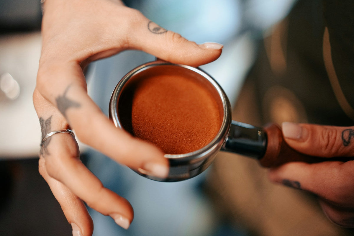 Hands holding espresso portafilter with espresso grounds in the puck
