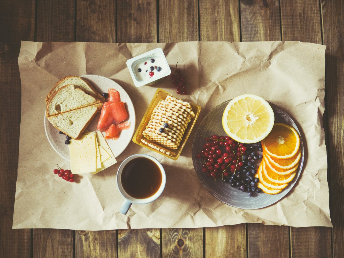 black coffee on a table surrounded by berries, cheese, crackers and yogurt