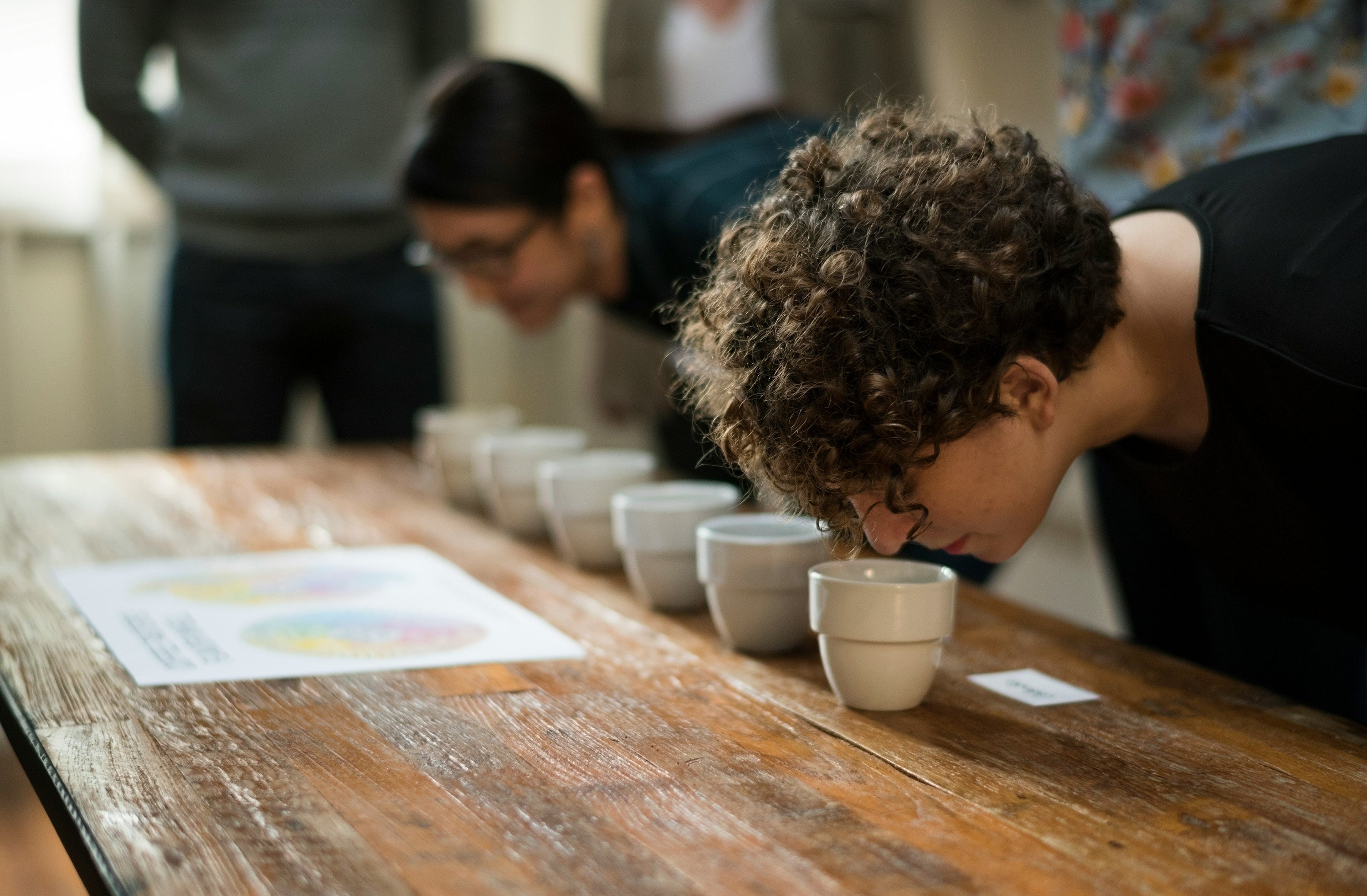 two people stooping to smell coffee as part of the coffee cupping process