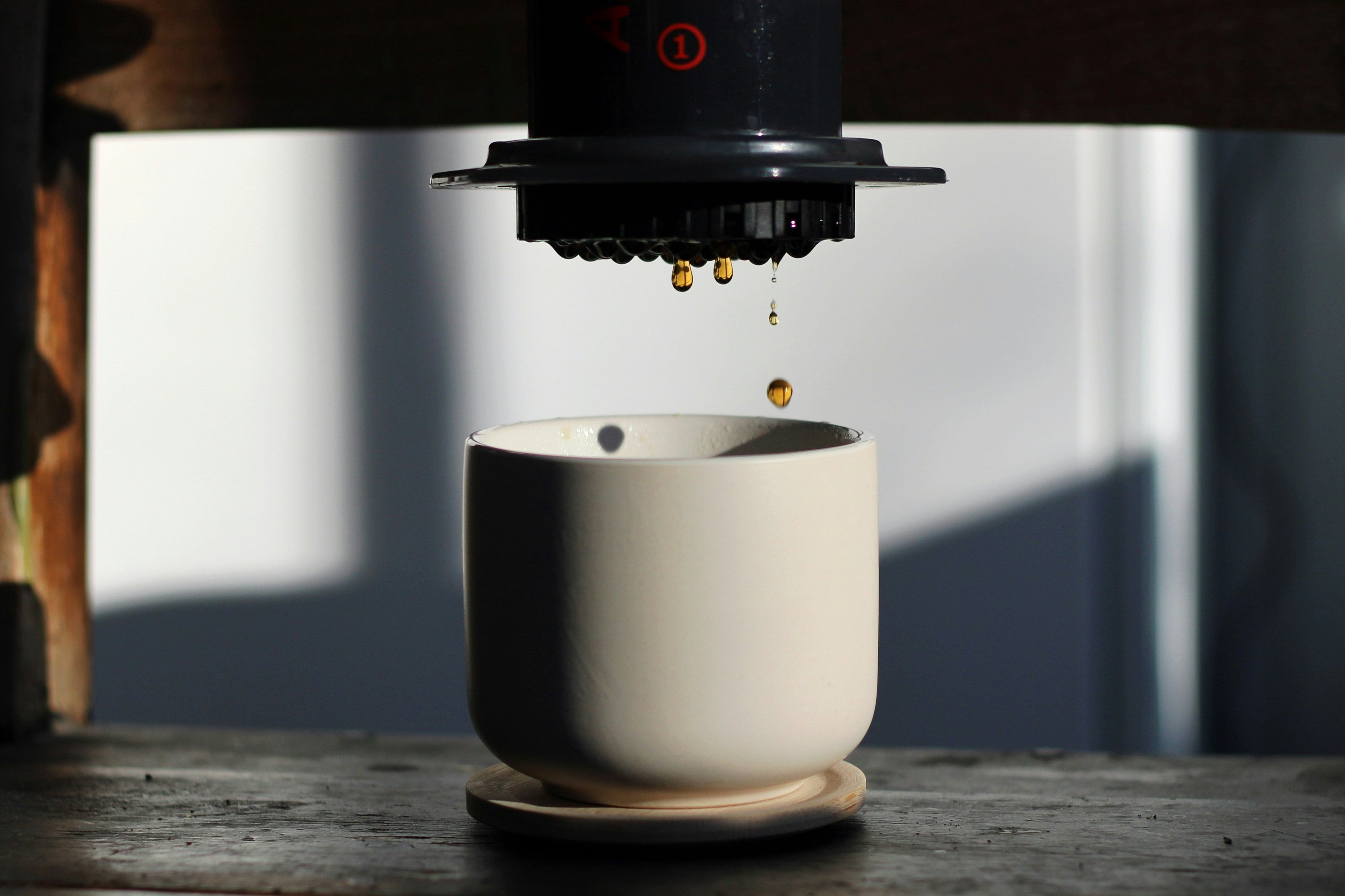 brewed coffee dripping into a white handleless coffee cup