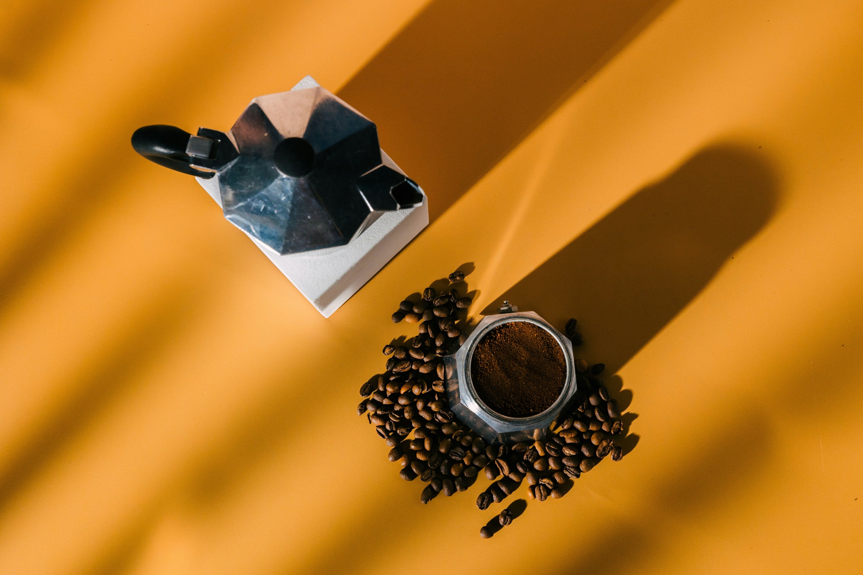 moka pot coffee maker on yellow background with coffee beans sitting around it