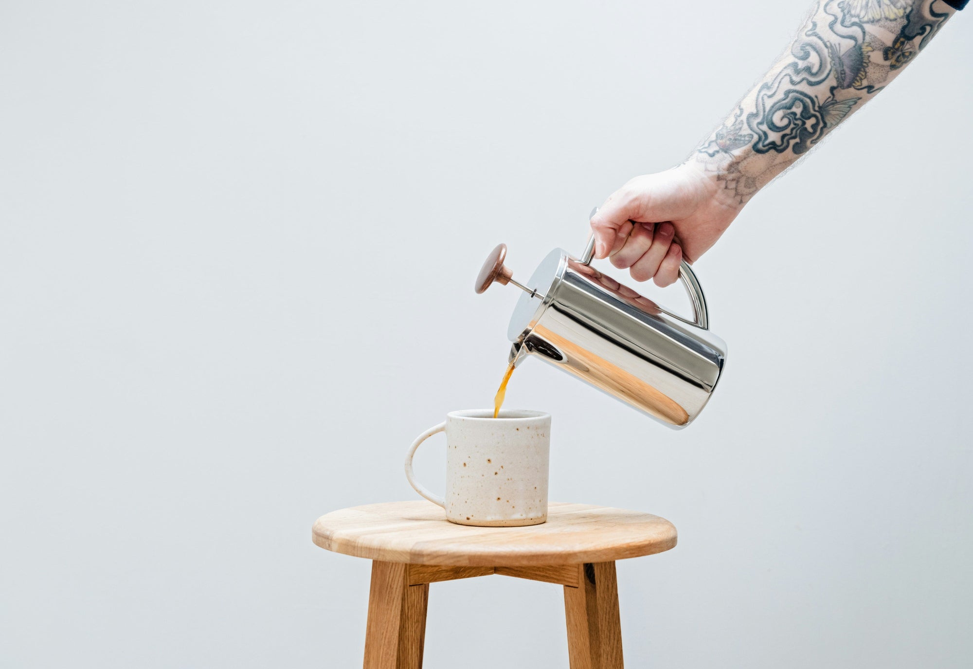 shiny metal french press coffee maker pouring coffee into a white coffee cup