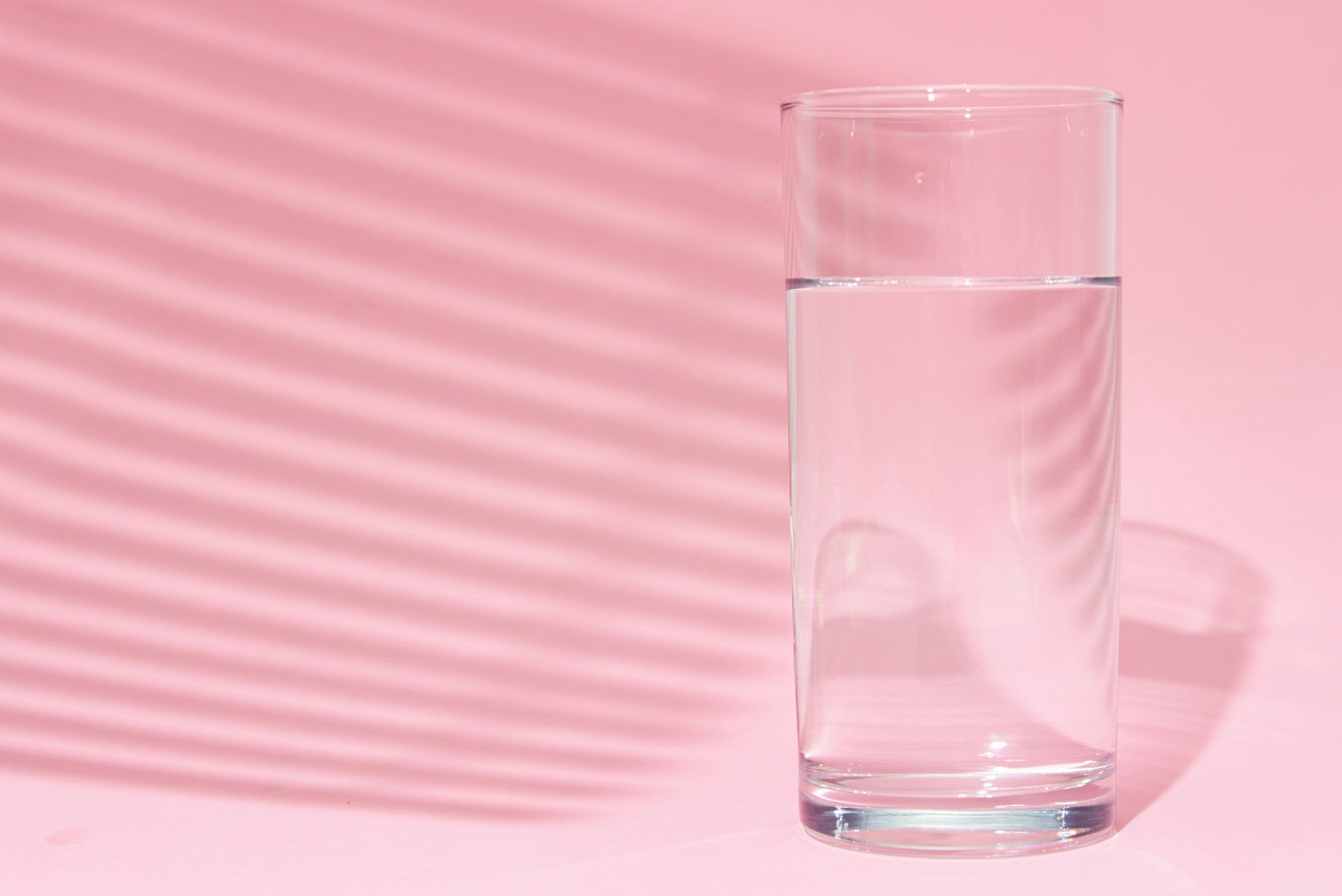 glass full of water against a pink background