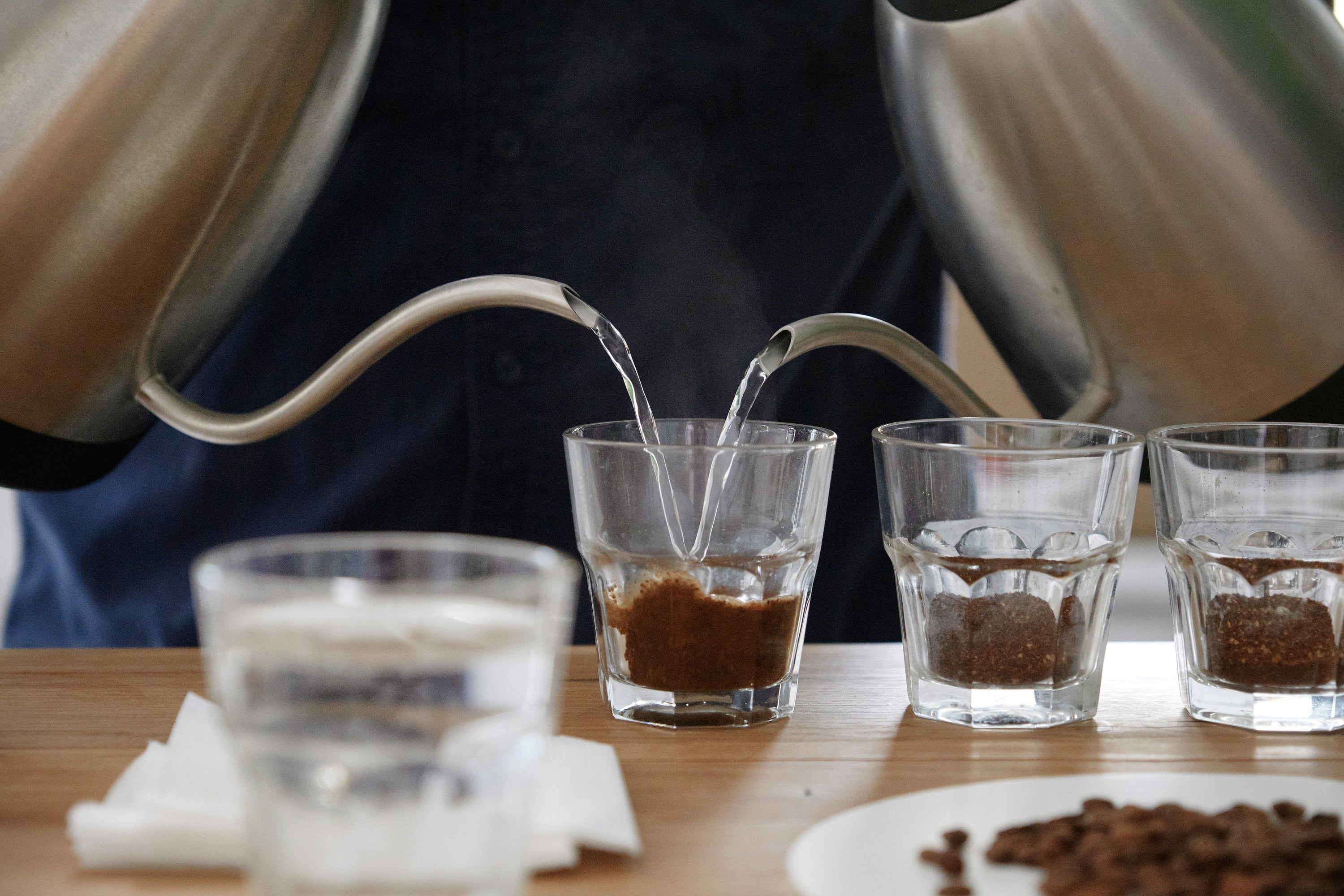 two gooseneck kettles pouring water into coffee glass