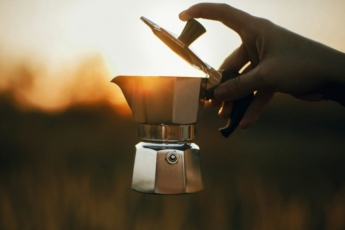 Moka pot coffee maker being held against a beautiful sunset
