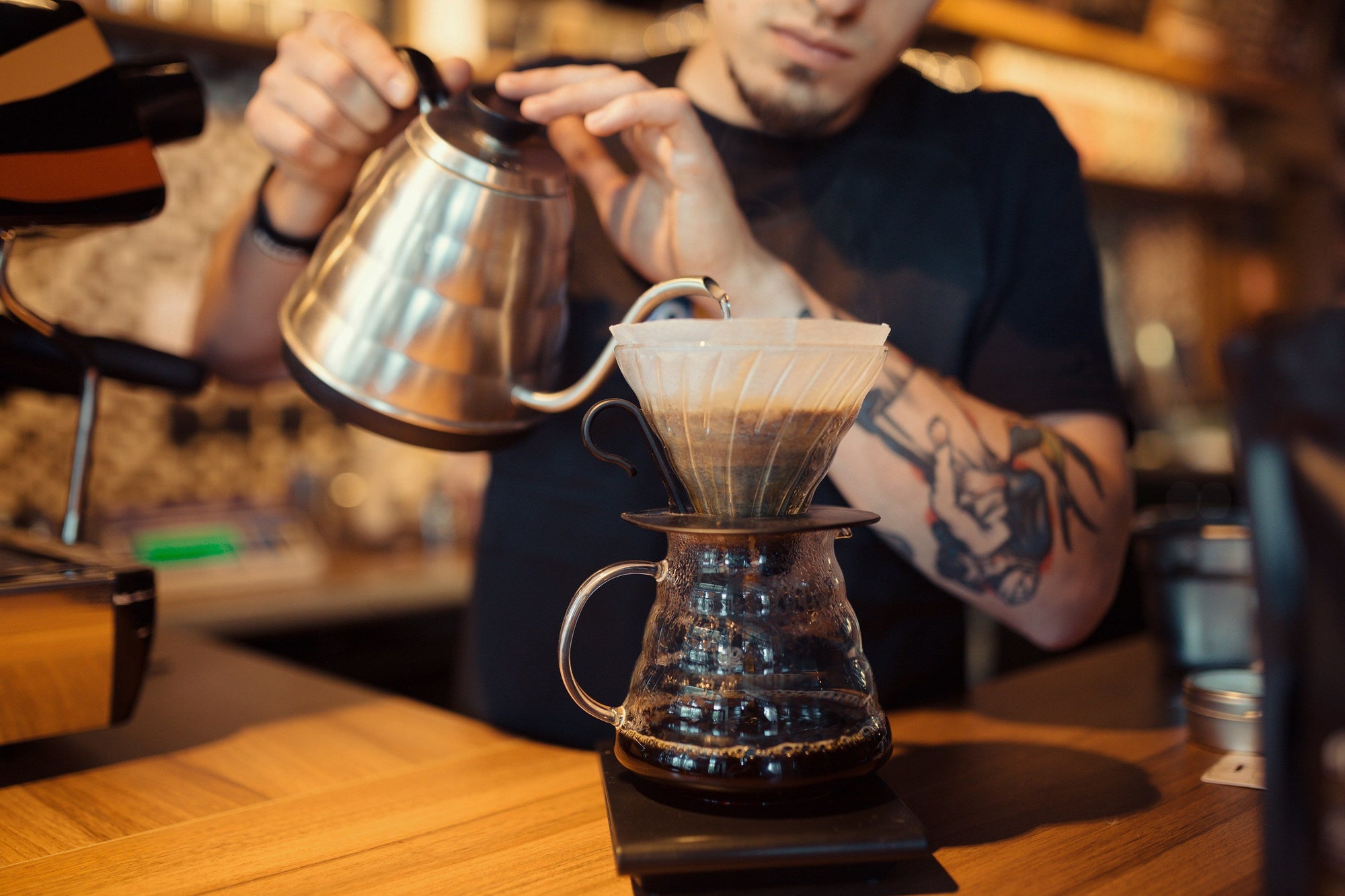 person pouring water from a gooseneck kettle into a coffee dripper
