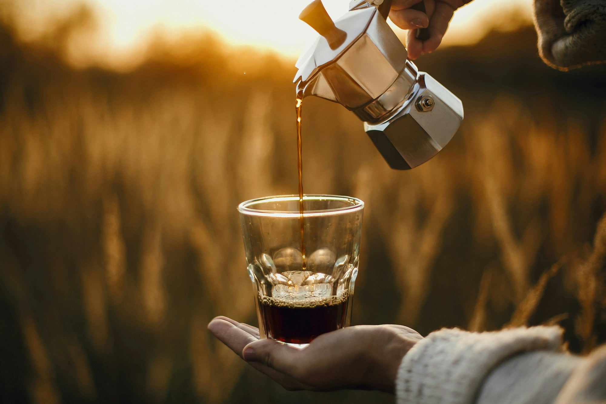 moka pot pouring coffee into glass outside in a field