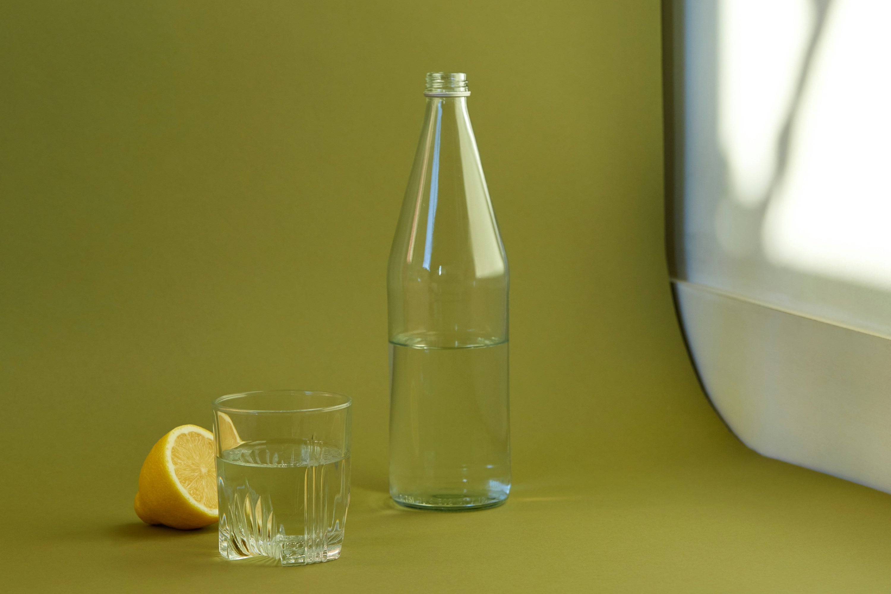 clear glass bottle and glass of water against dark green background