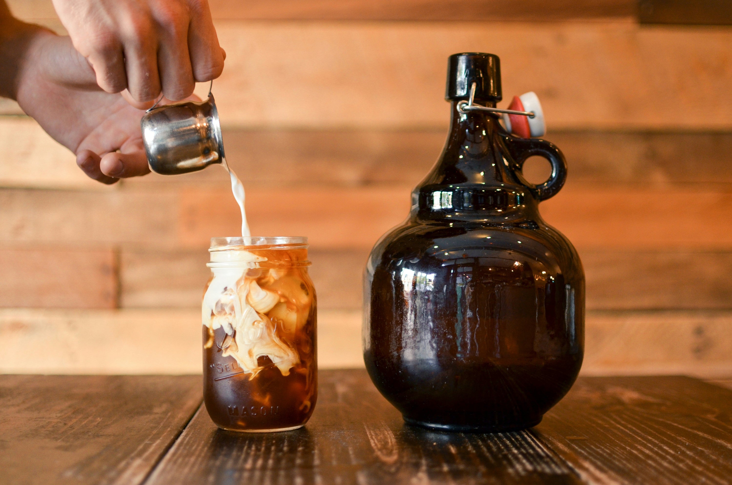 cold brew coffee with cream poured into it, on wooden countertop