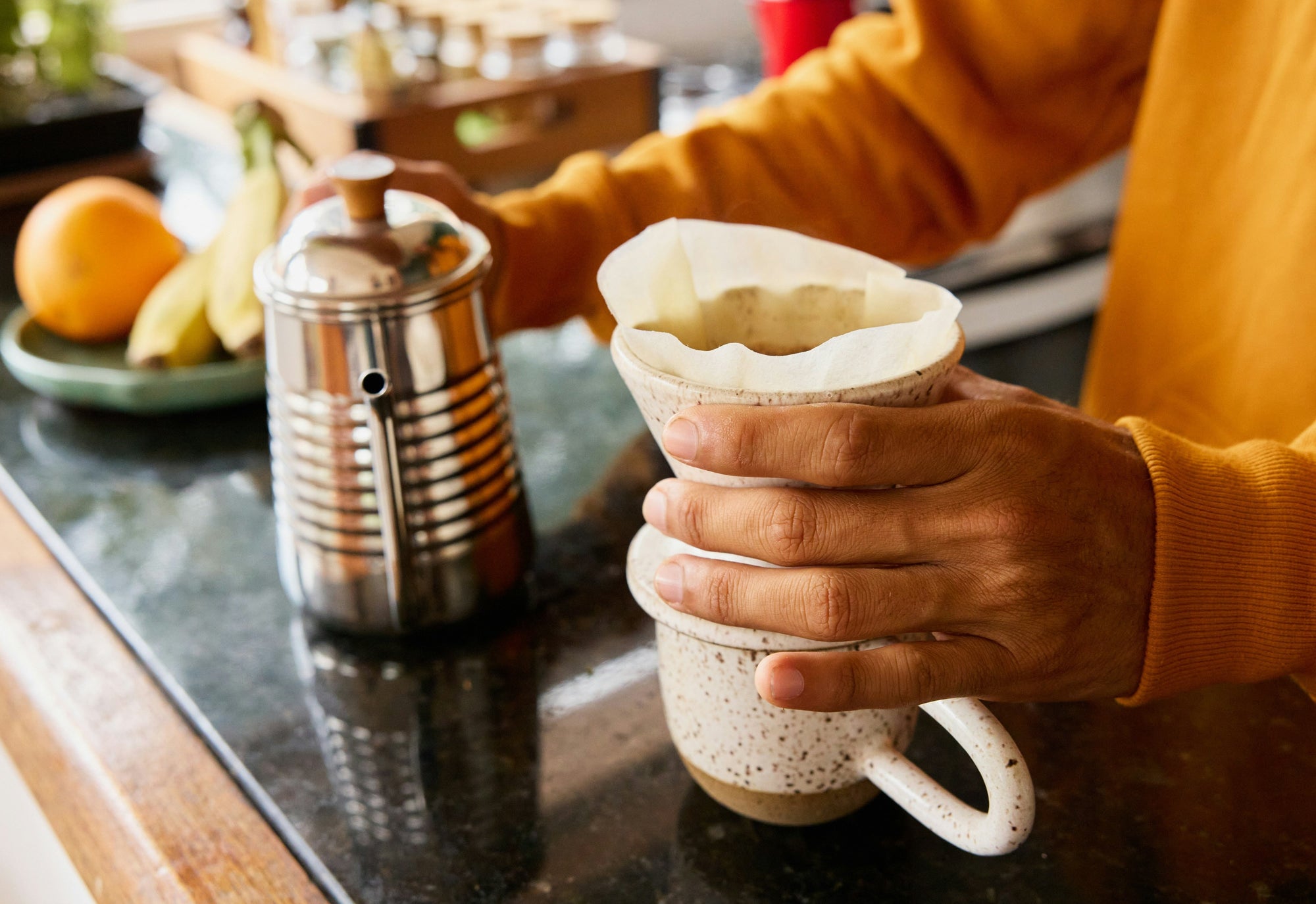 Pour over coffee being made in kitchen by person wearing orange sweater
