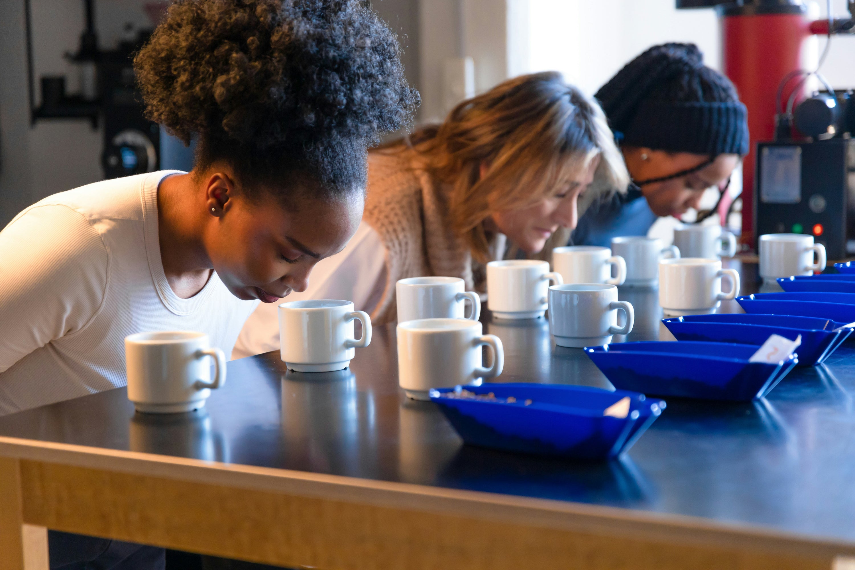three people stooping down to smell freshly brewed coffee as part of coffee cupping process