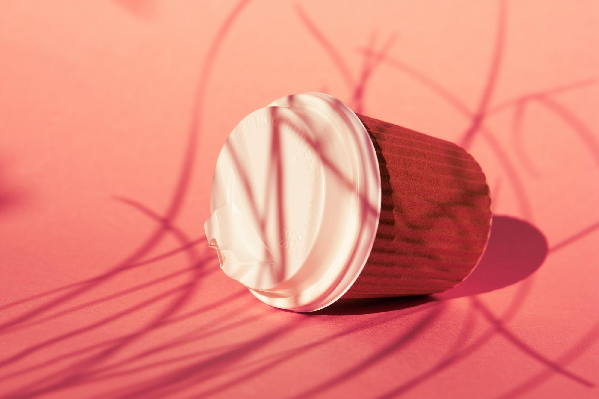 disposable coffee cup that has fallen over, lying on pink gradient background
