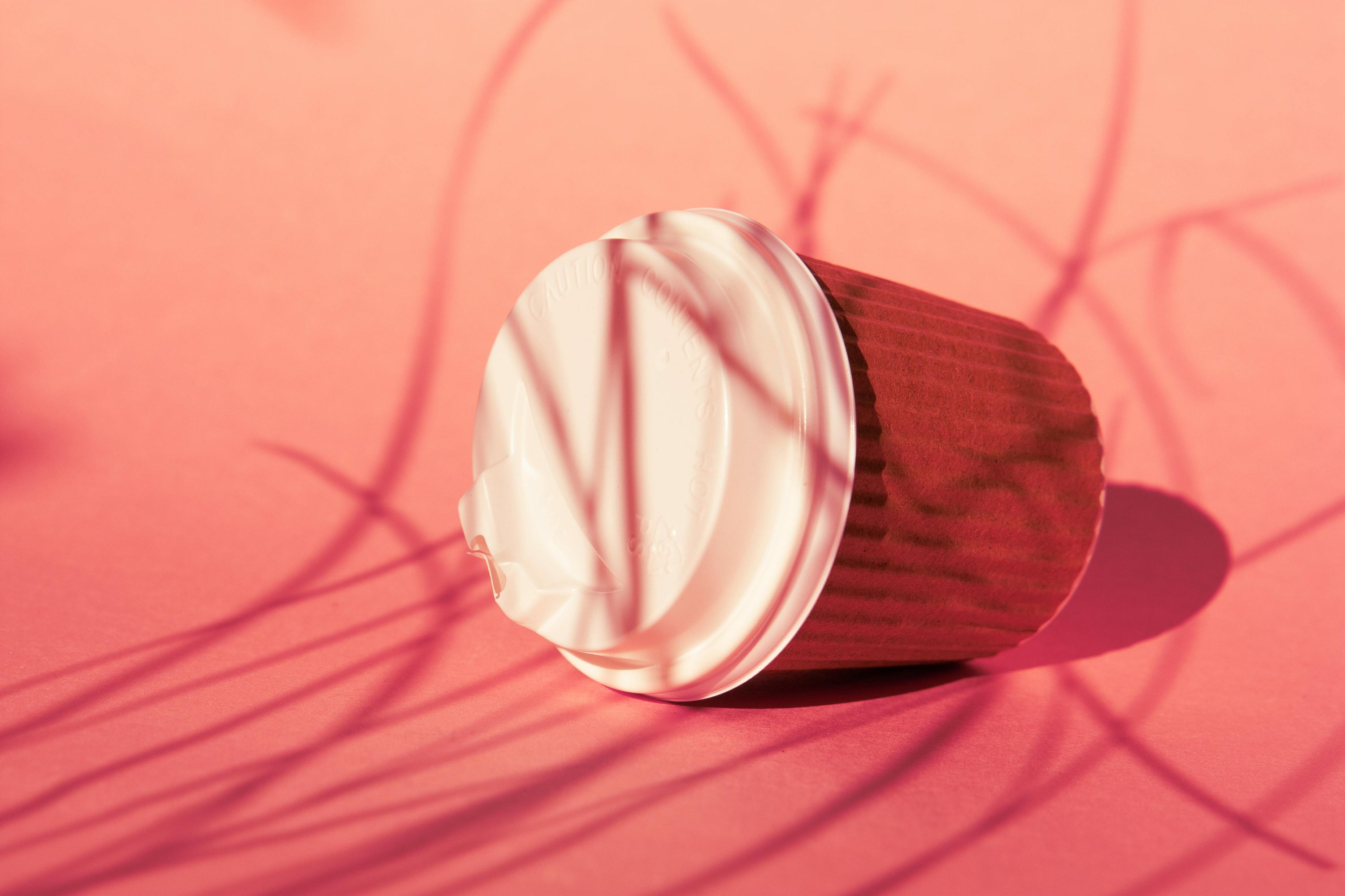 disposable coffee cup that has fallen over, lying on pink gradient background