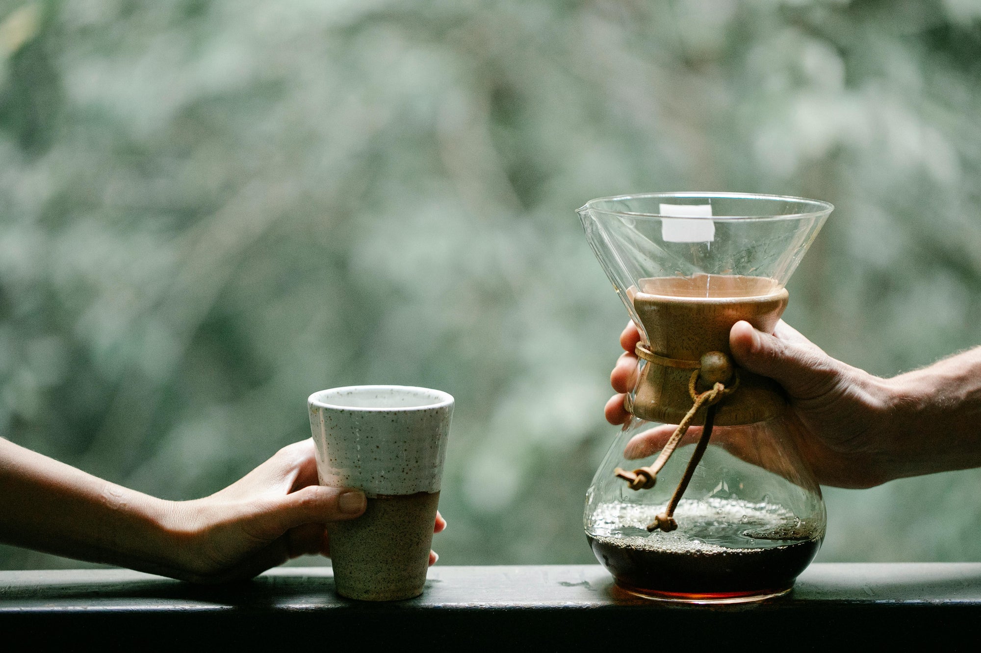 chemex coffee dripper sitting on windowsill next to a coffee cup