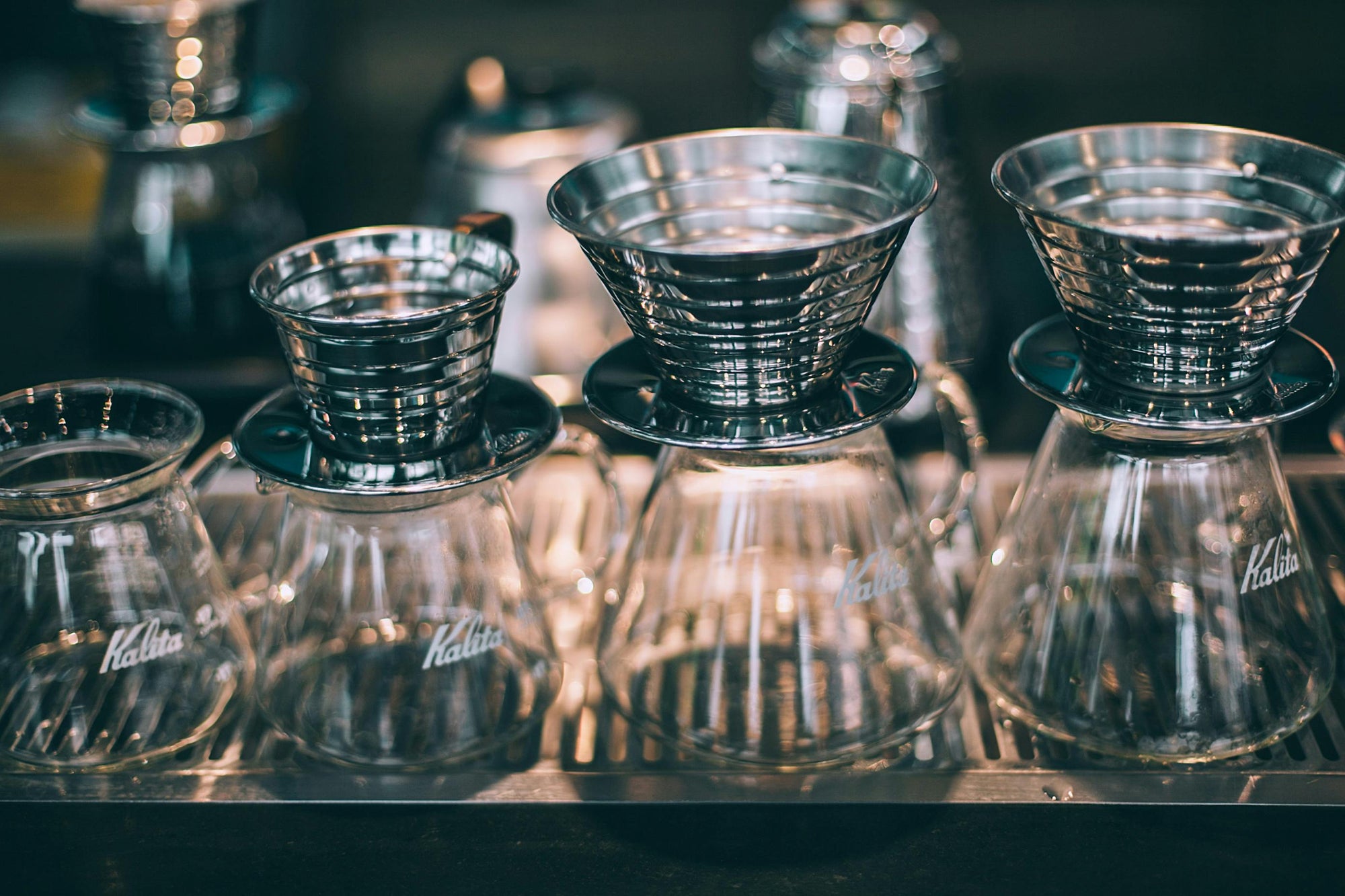 various sizes of Kalita Wave coffee dripper sitting on top of clear glass coffee carafes