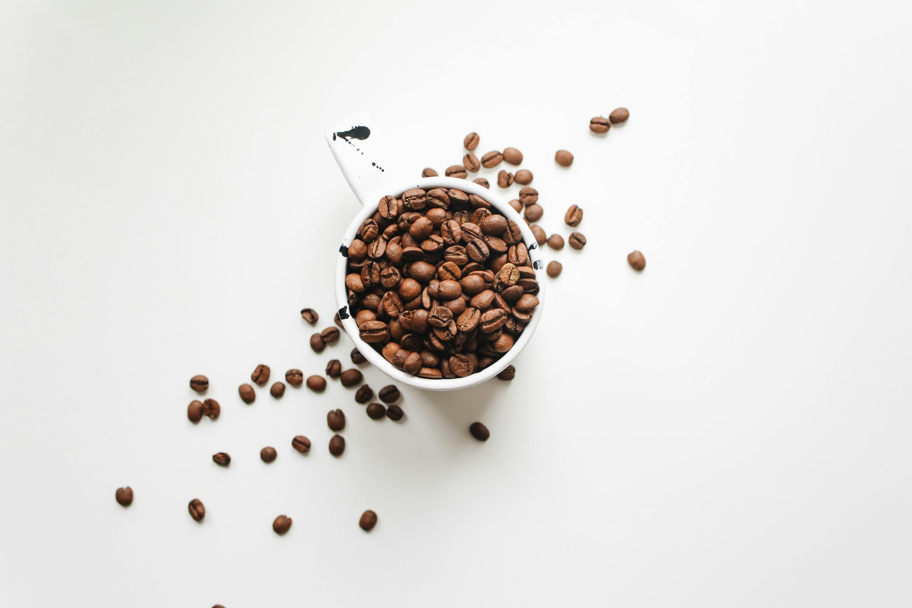 coffee beans being stored in a coffee mug and spilling out on to a white tabletop