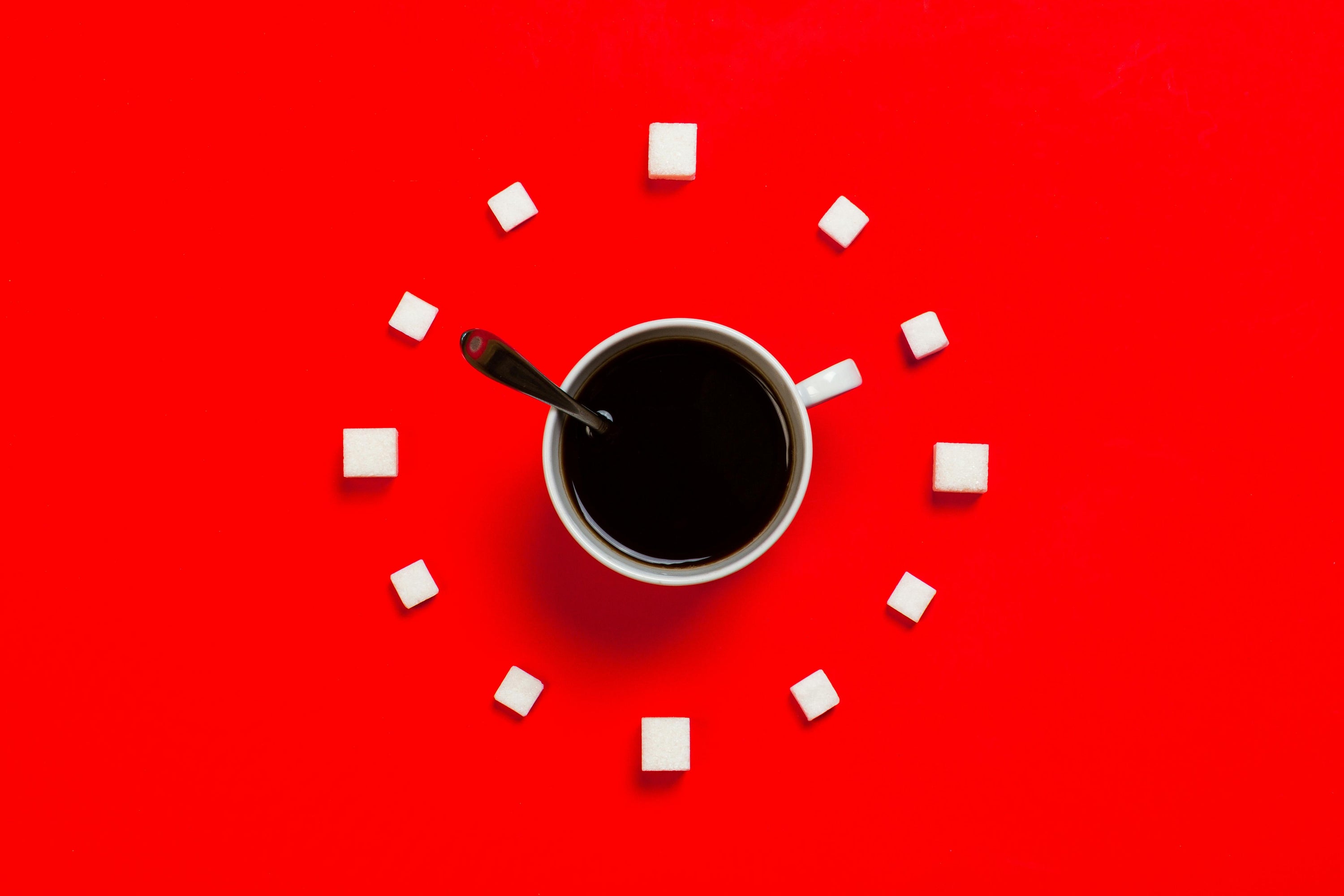 coffee cup and spoon making the hands of a clock, and sugar cubes in a circle formed to make a clock shape
