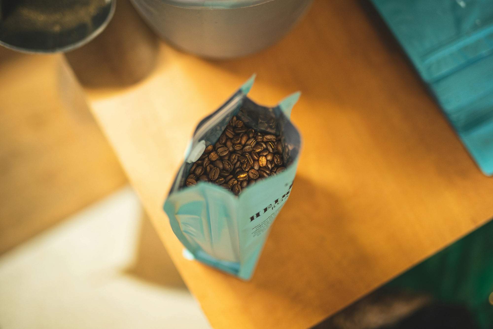 teal colored coffee bag open and revealing coffee whole coffee beans inside
