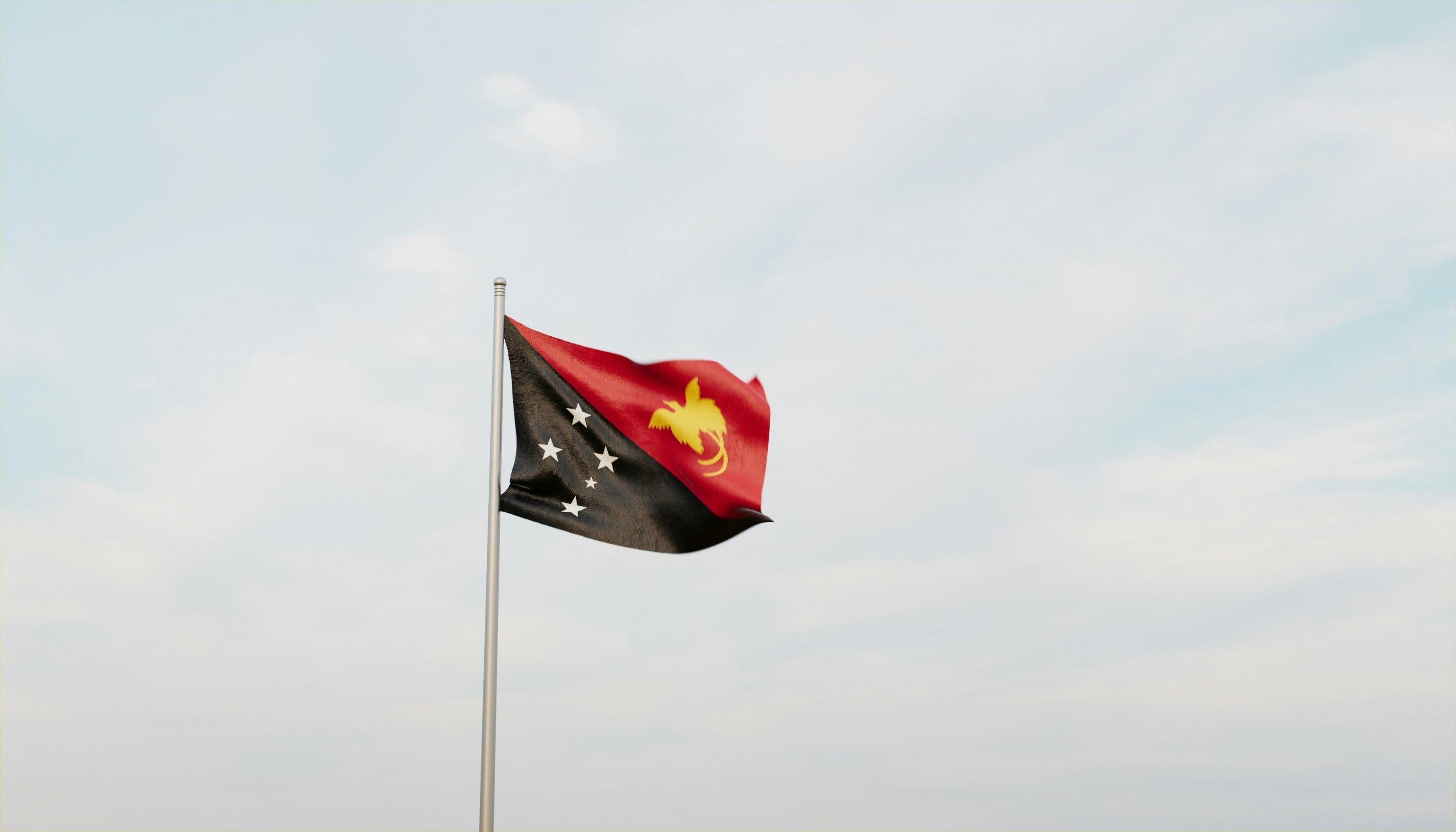 Papua New Guinea flag flying against a clouded blue sky