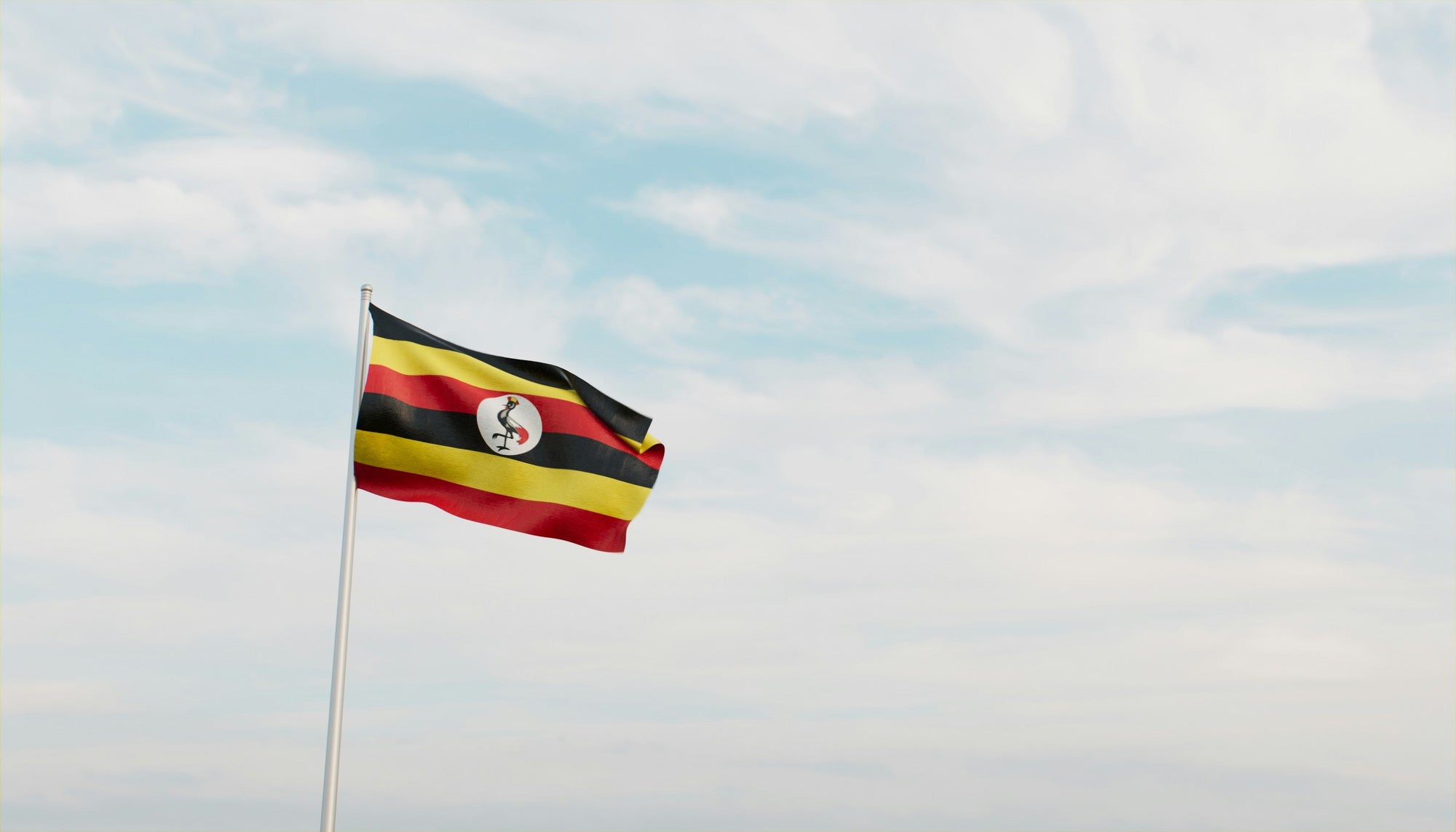 Uganda flag fluttering in the wind against a clouded blue sky