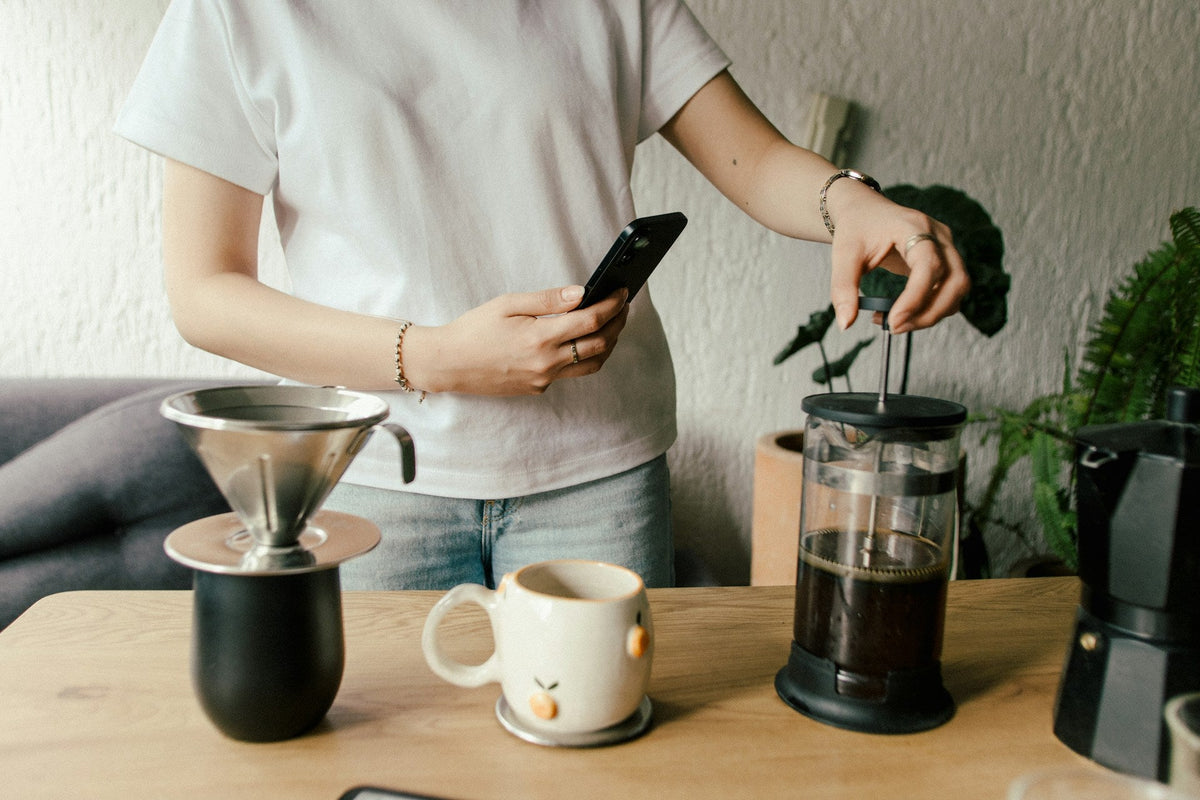 Person pushing down plunger on French Press coffee maker on wooden countertop
