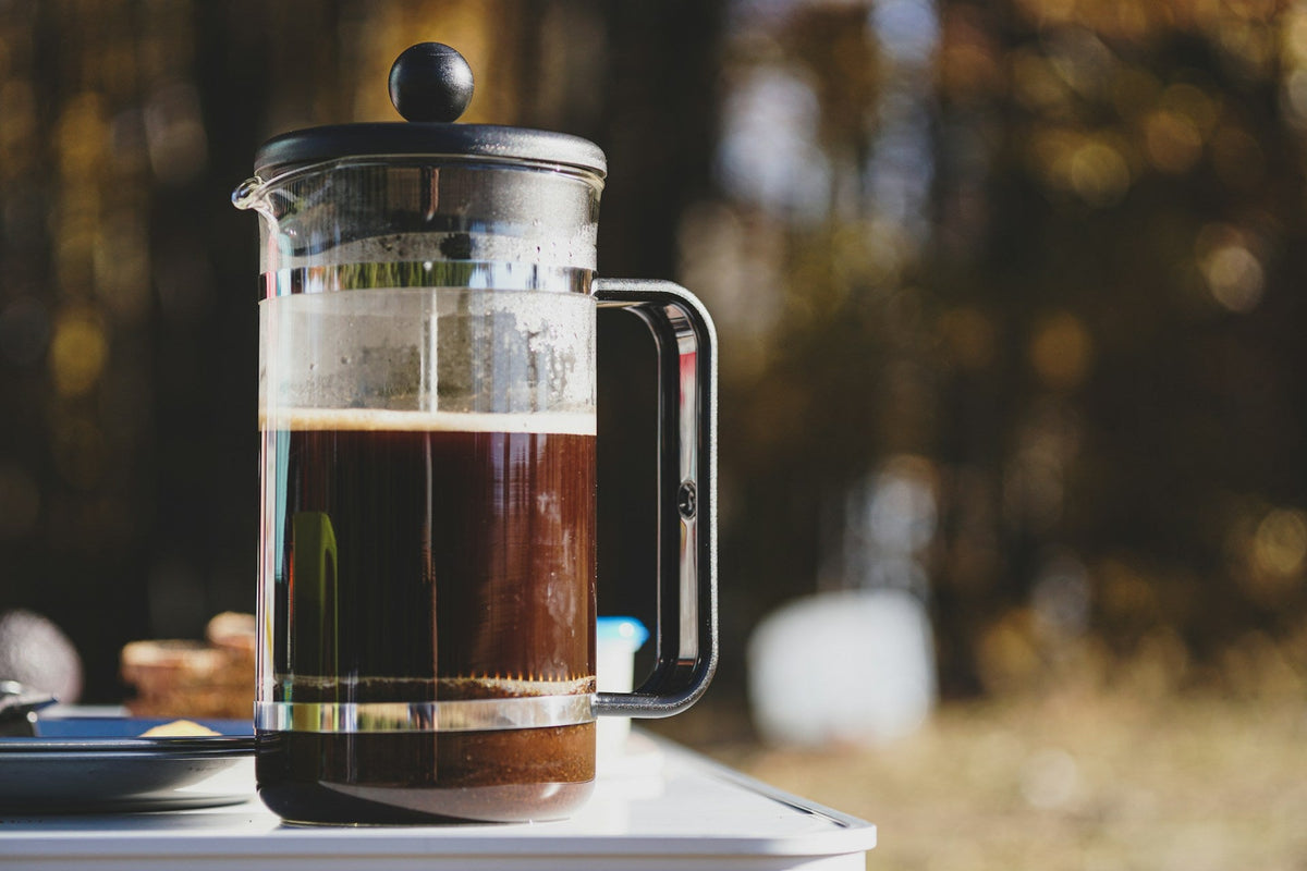French press full of coffee on picnic table