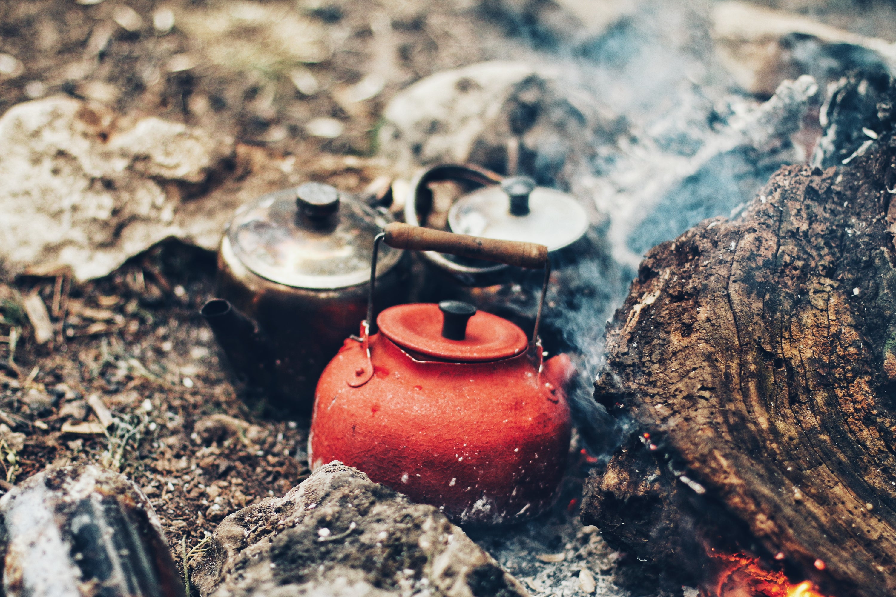 3 kettles on embers of wood campfire