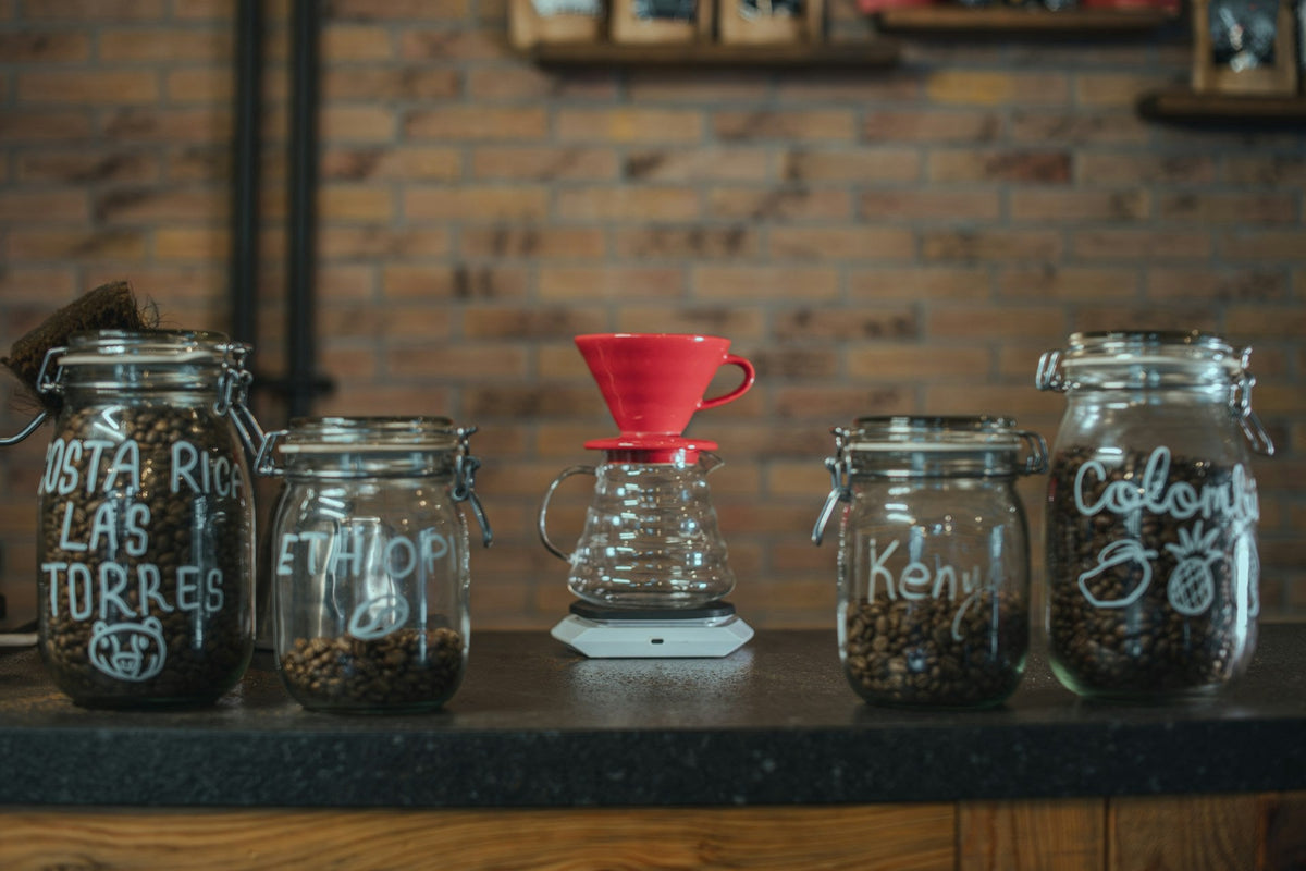 V60 dripper surrounded by glass jars holding coffee beans