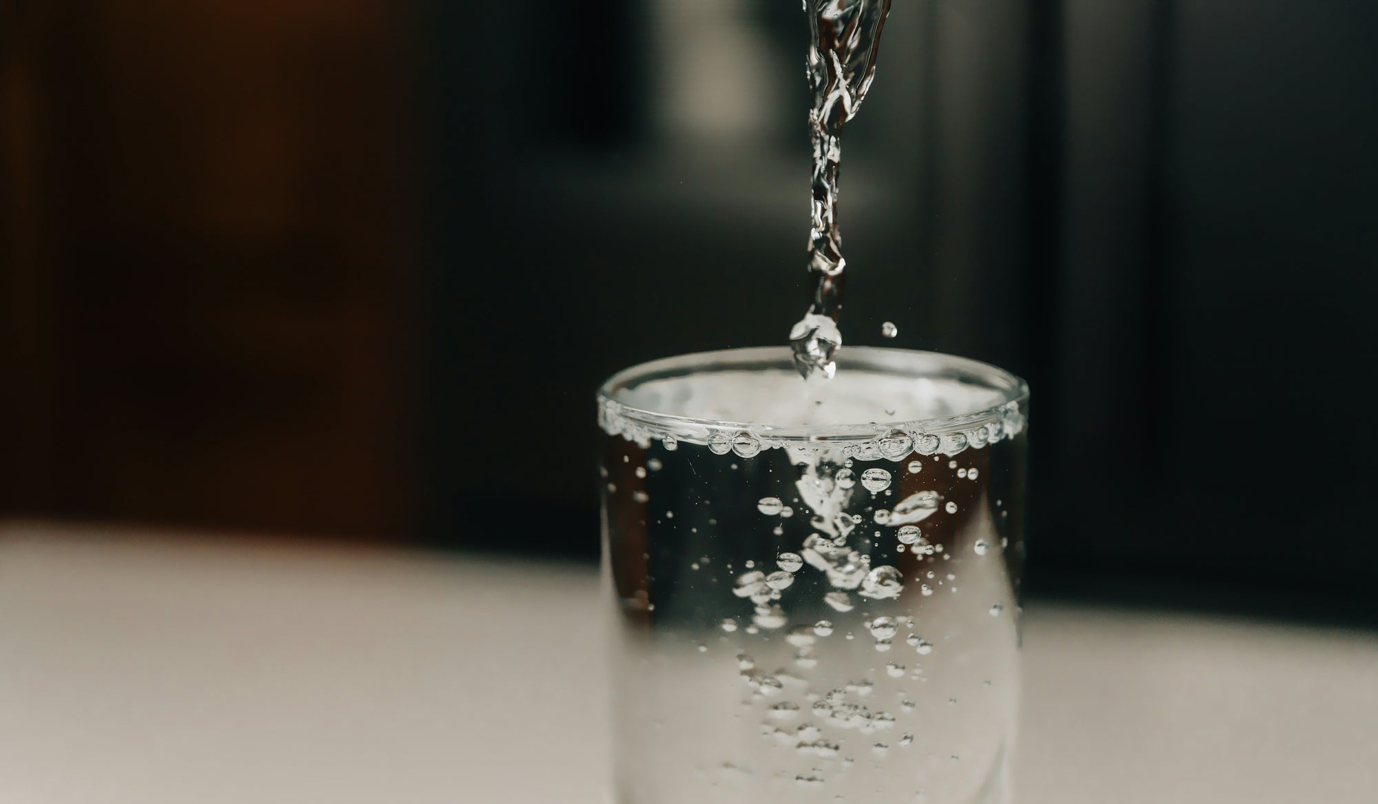 clear water dripping into glass against dark background