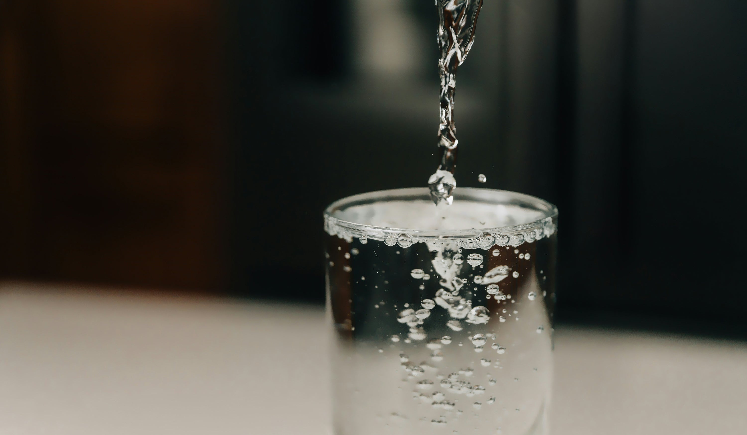clear water dripping into glass against dark background